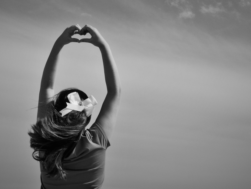 a woman facing the sky putting a heart shape sign up in the air